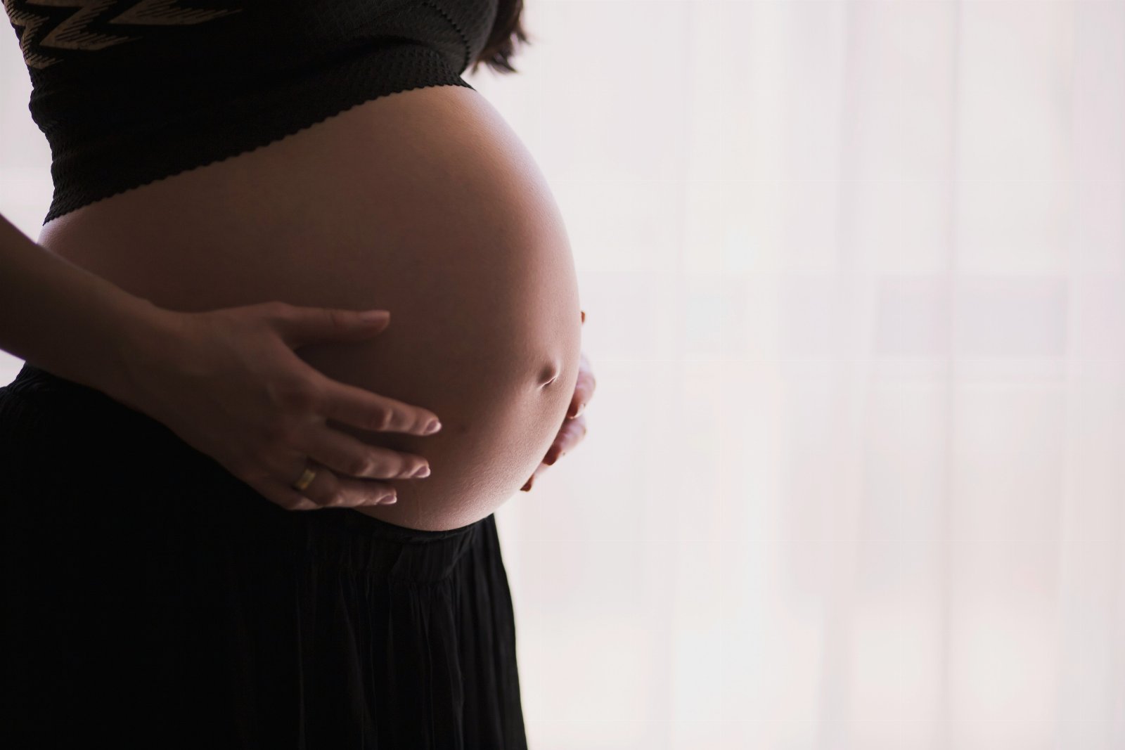 Gestante acariciando a barriga em um ambiente iluminado por luz natural.
